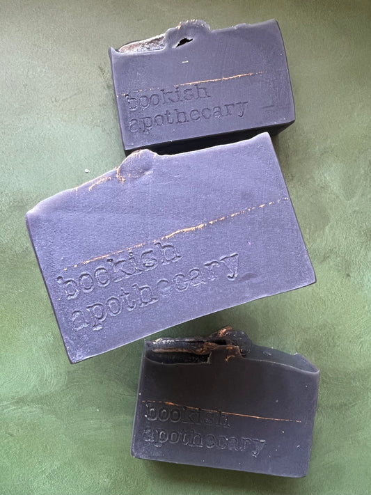 Three bars of dark purple soap stamped with bookish apothecary branding.