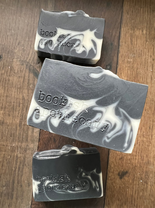 Three bars of black and white soap with 'bookish apothecary' branding on a wooden surface