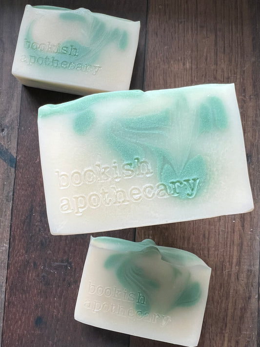 Three bars of white soap with green swirls with 'bookish Apothecary' branding on a wooden surface.