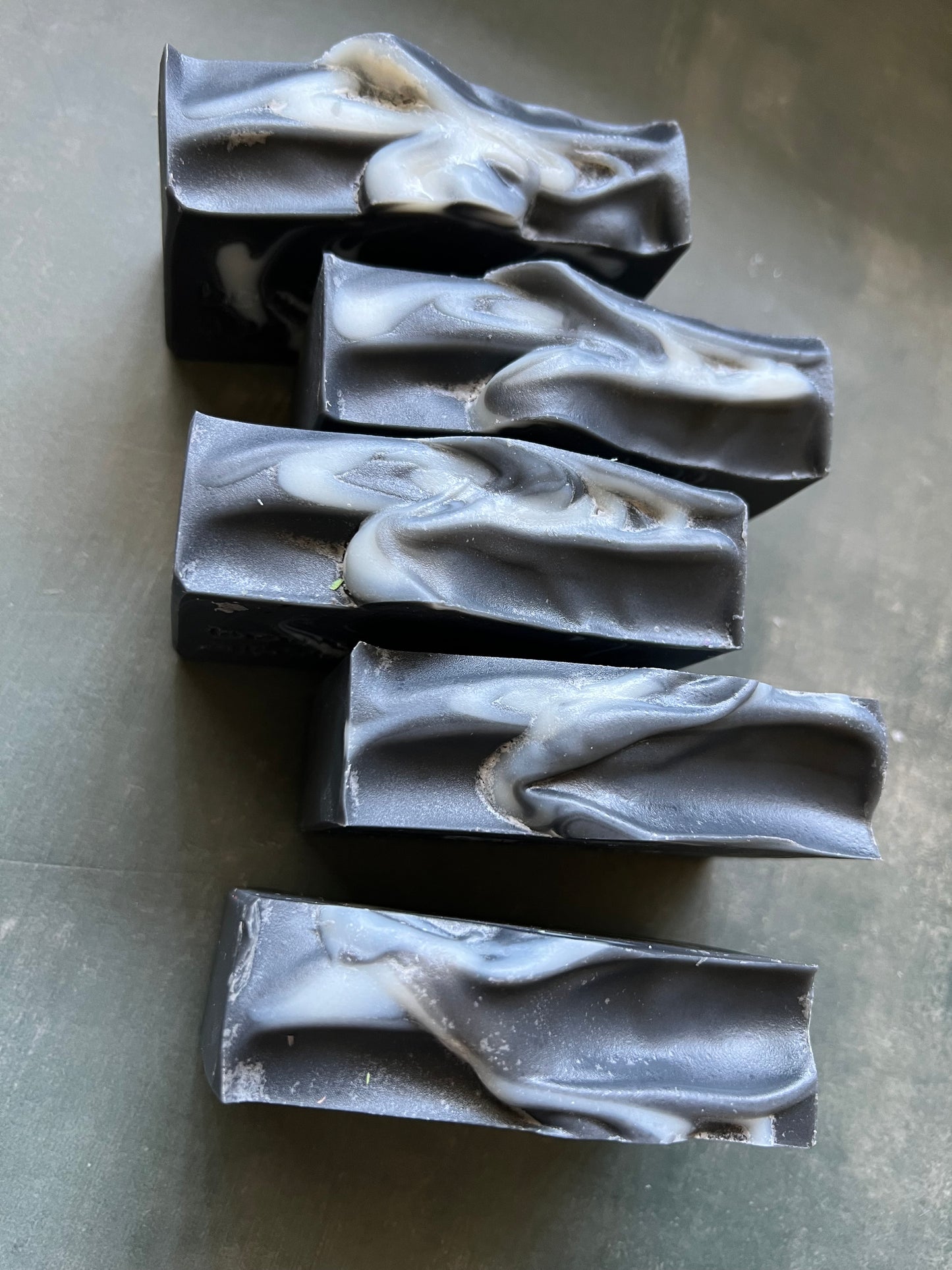 Five bars of black soap with unique shapes on a gray surface