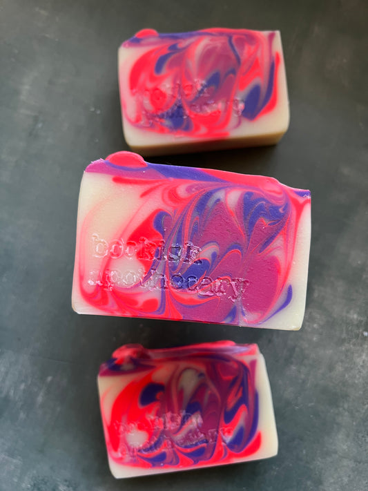 Three bars of soap with pink and purple swirls on a dark surface