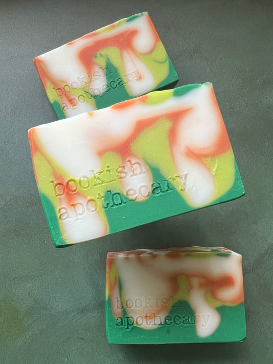 Three bars of swirled soaps comprised of orange, chartreuse and green soap stamped with bookish apothecary branding.