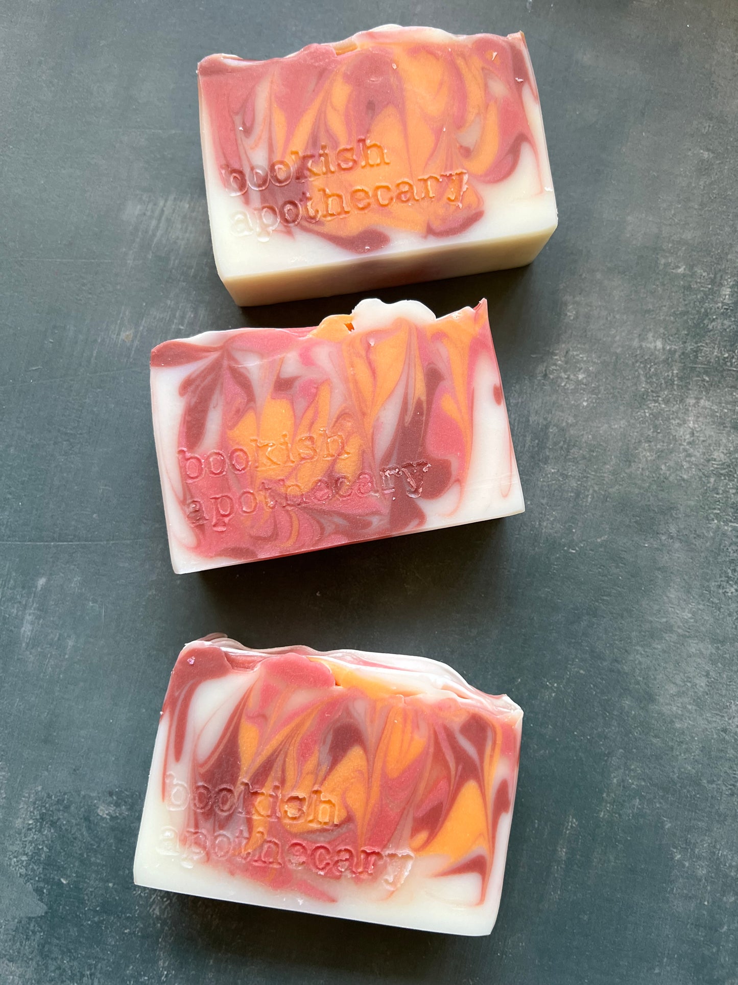 Three bars of soap with a marbled design on a dark surface