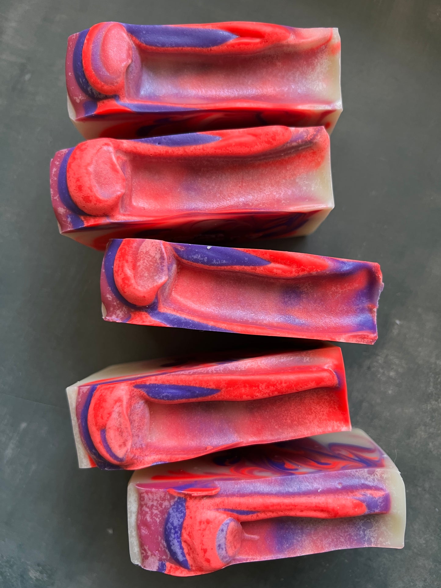 Five bars of red and purple soap arranged on a dark surface
