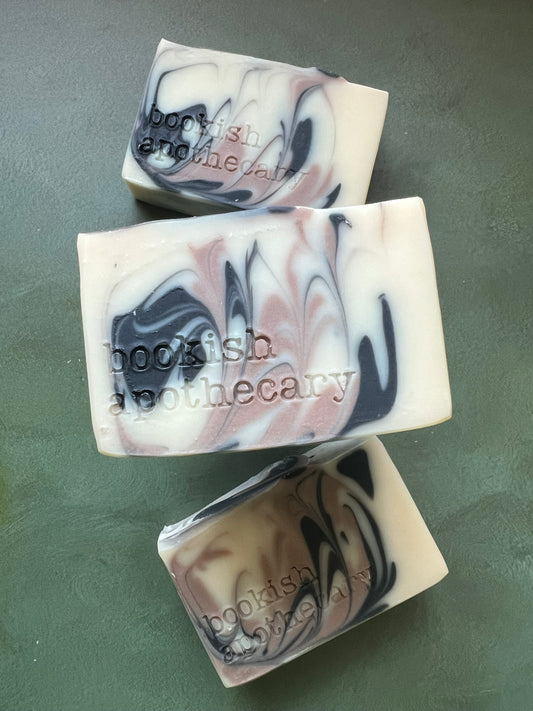Three bars of white soap with black and tan swirls stamped with bookish apothecary branding.