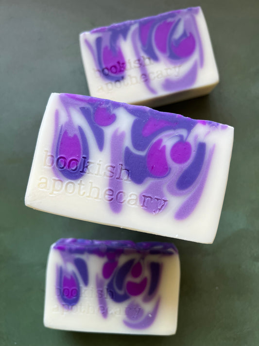 Three bars of white soap with purple swirls stamped with bookish apothecary branding.