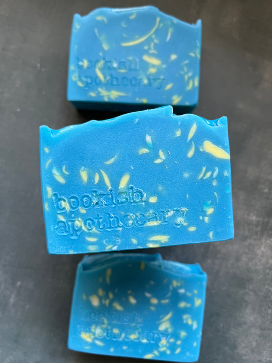Three blue soap bars with yellow specks on a dark gray background