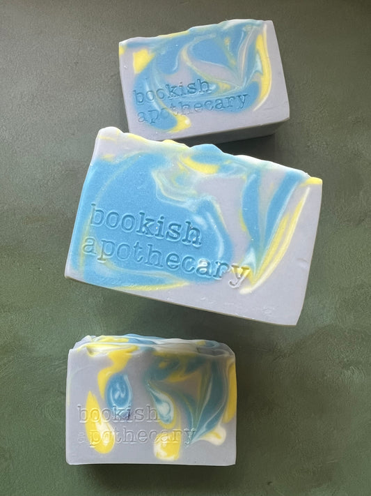 Three bars of gray soap with blue, yellow and white swirls stamped with bookish apothecary branding.