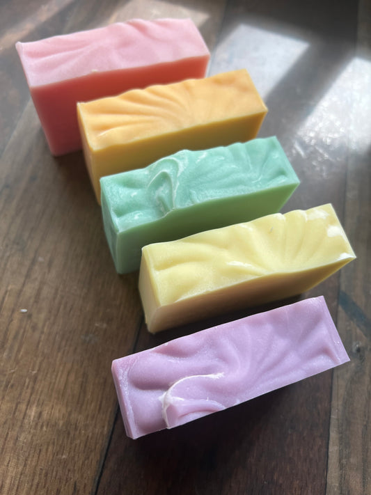 Five rectangular bars of soap in different colors on a wooden surface