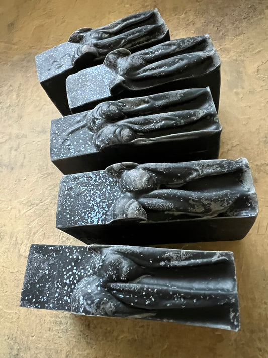 Five rectangular dark gray to black bars with raised organic sculptural tops, arranged on a textured tan surface.