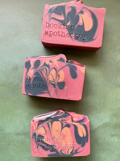Three bars of red soap with black and bronze swirls stamped with bookish apothecary branding.
