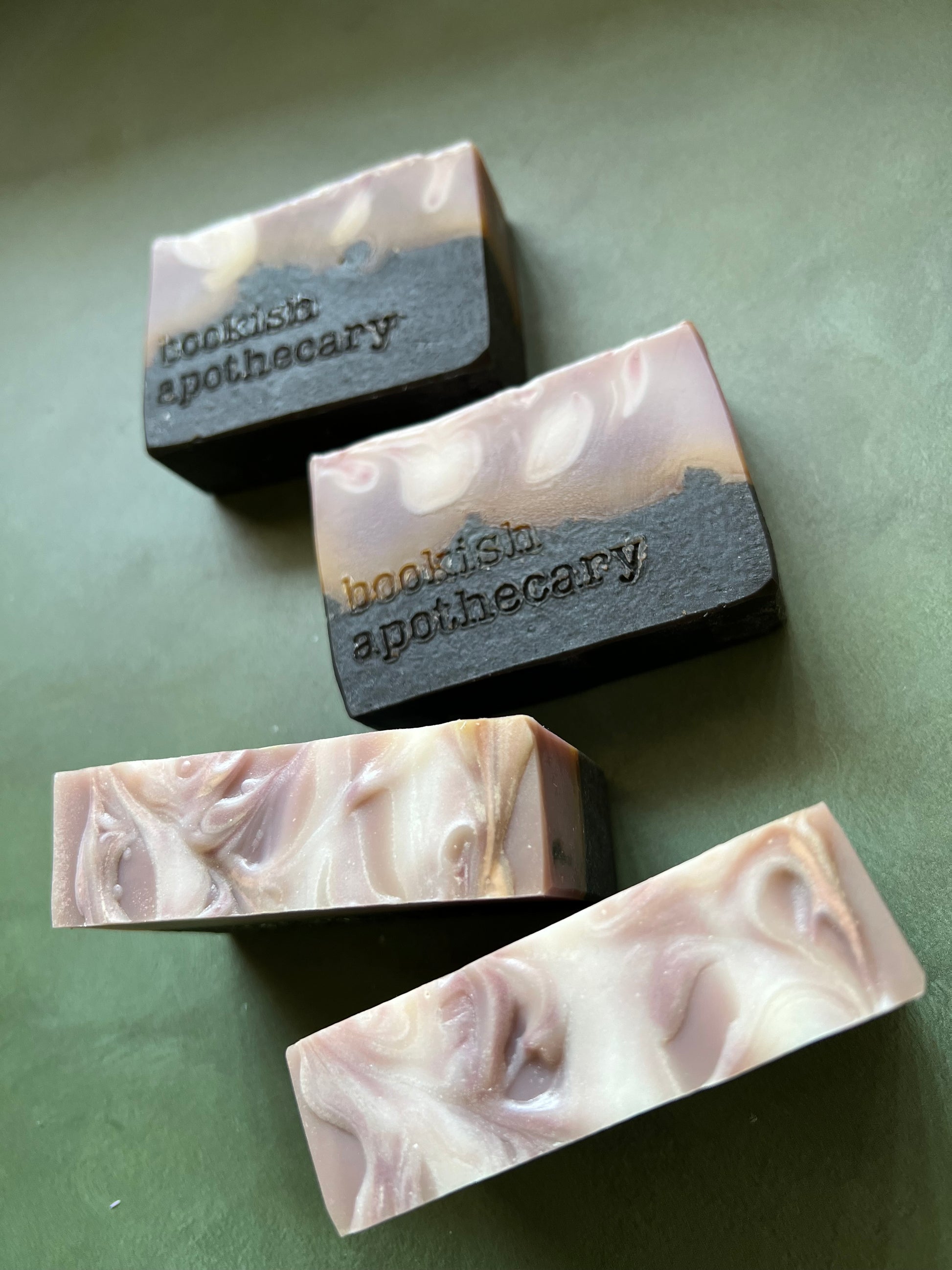 four bars of  soap with a tan top and black bottom stamped with bookish apothecary branding.
