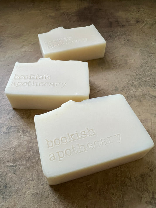 Three off-white rectangular bars of soap with embossed vertical text reading 'bookish apothecary' resting on a textured brown surface.