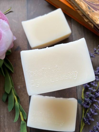 Three bars of soap with embossed branding on a wooden surface with lavender and greenery.