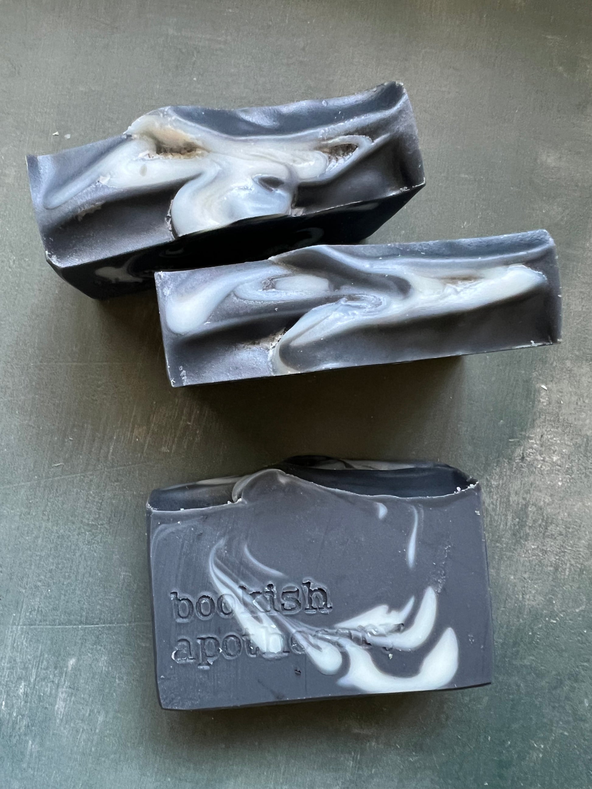 Three bars of soap with a marbled design on a gray surface, branded 'bookish Apothecary'.