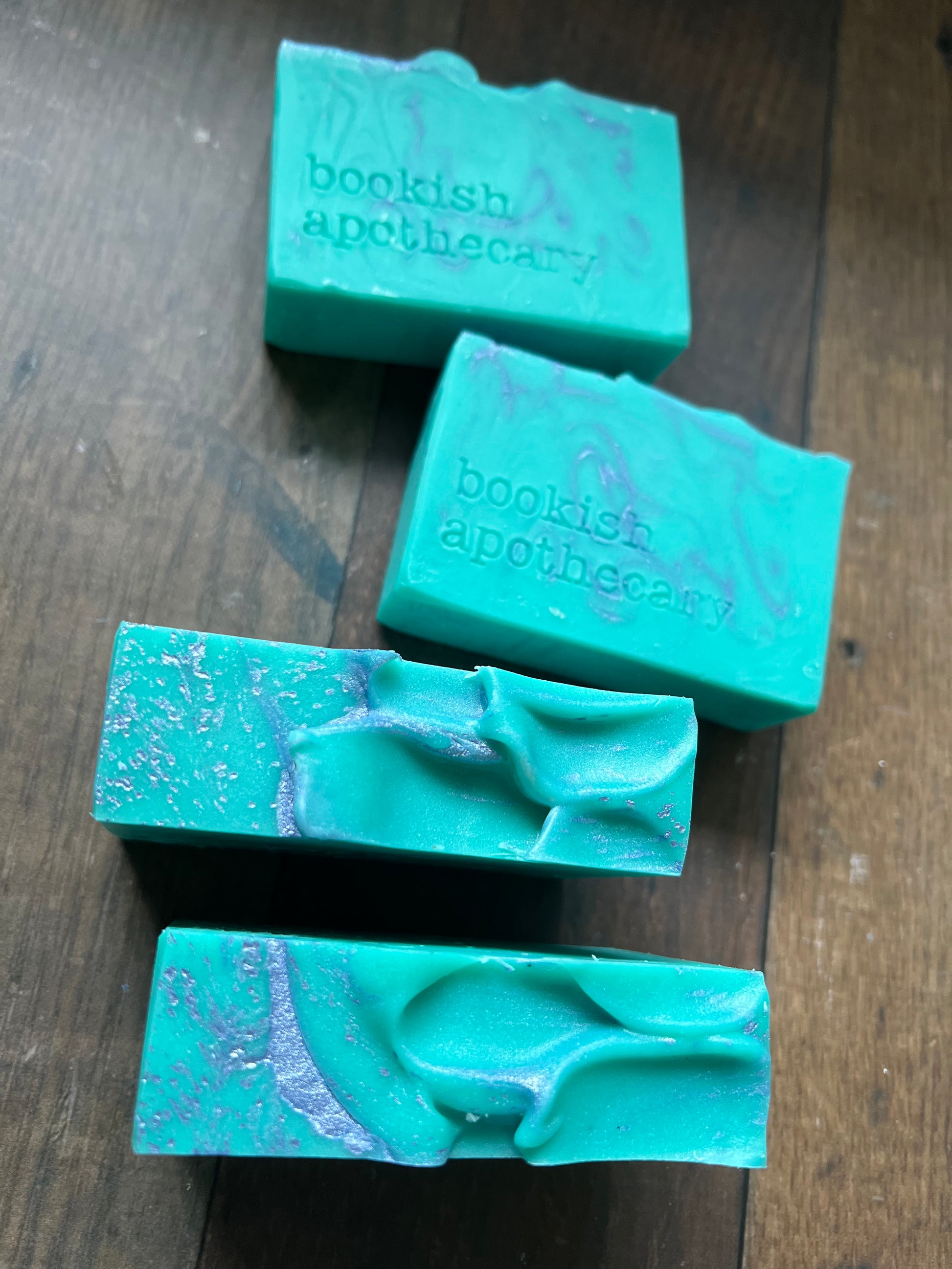 Four green soap bars with 'bookish apothecary' branding on a wooden surface.