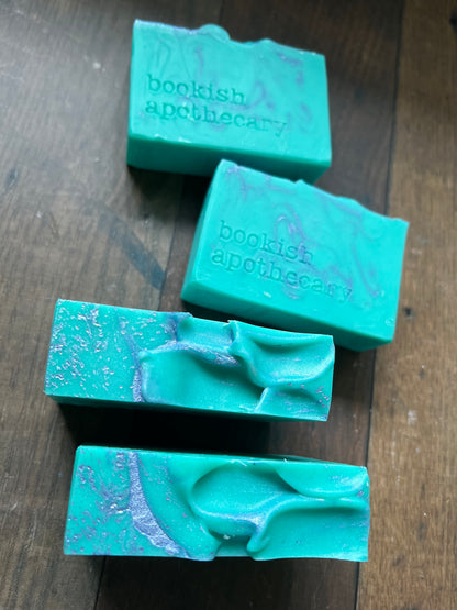 Four green soap bars with 'bookish apothecary' branding on a wooden surface.