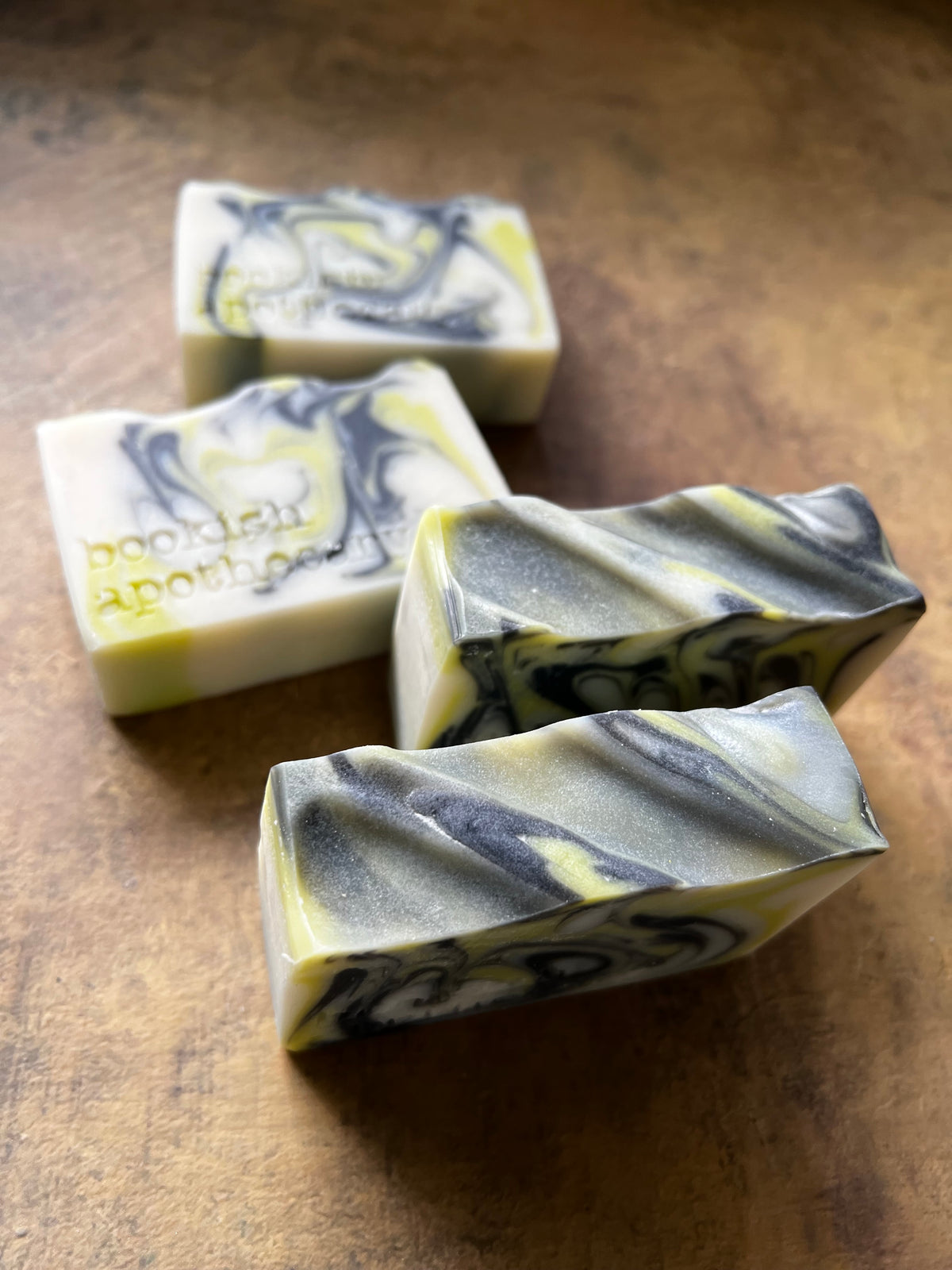Four artisanal marbled soap bars with black, gray, and yellow swirls, arranged on a rustic brown wooden surface. 