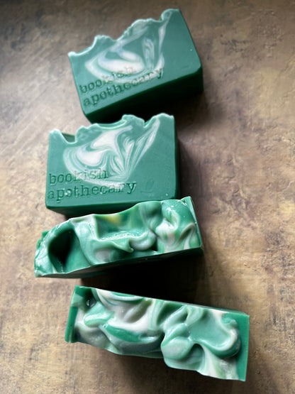 Four handmade green soap bars with white swirls are arranged diagonally on a textured brown surface.