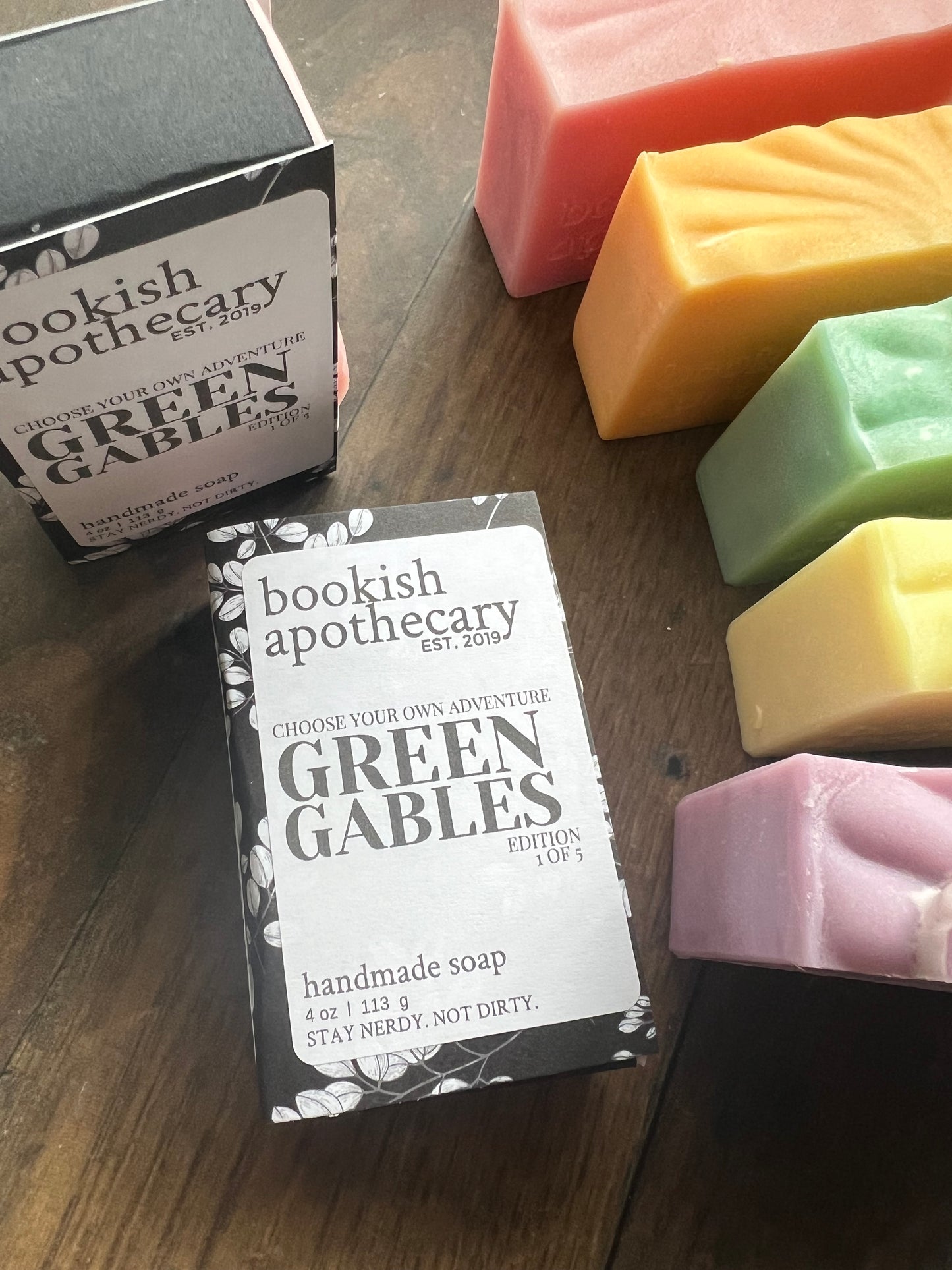 Green Gables handmade soap packaging on a wooden surface with colorful soap bars in the background.