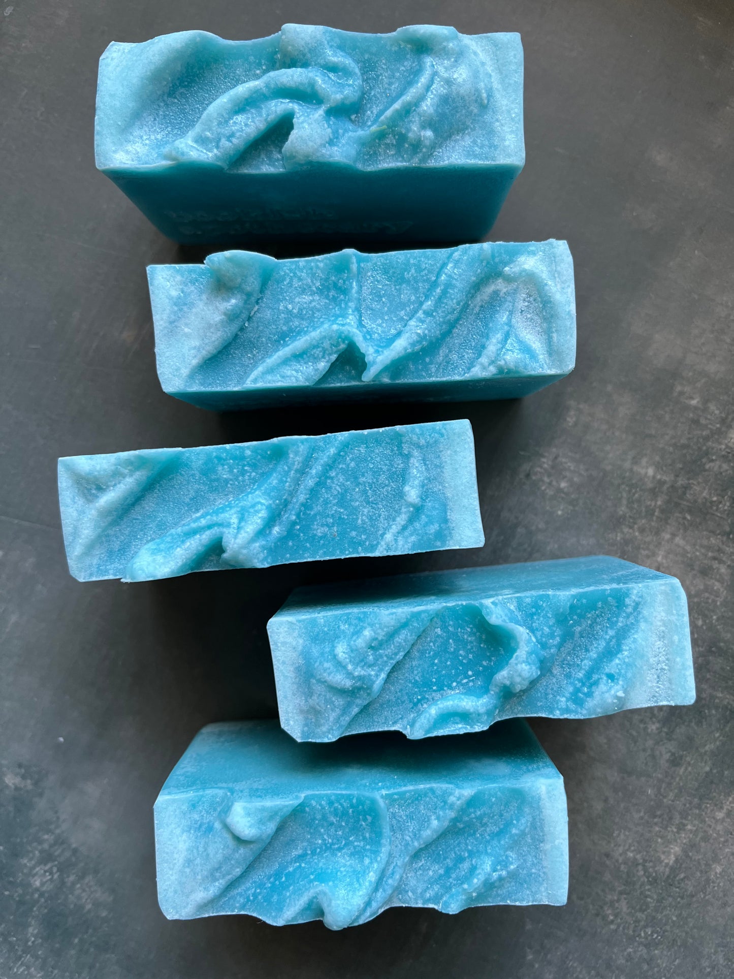 Five blue marbled soap bars on a dark gray surface