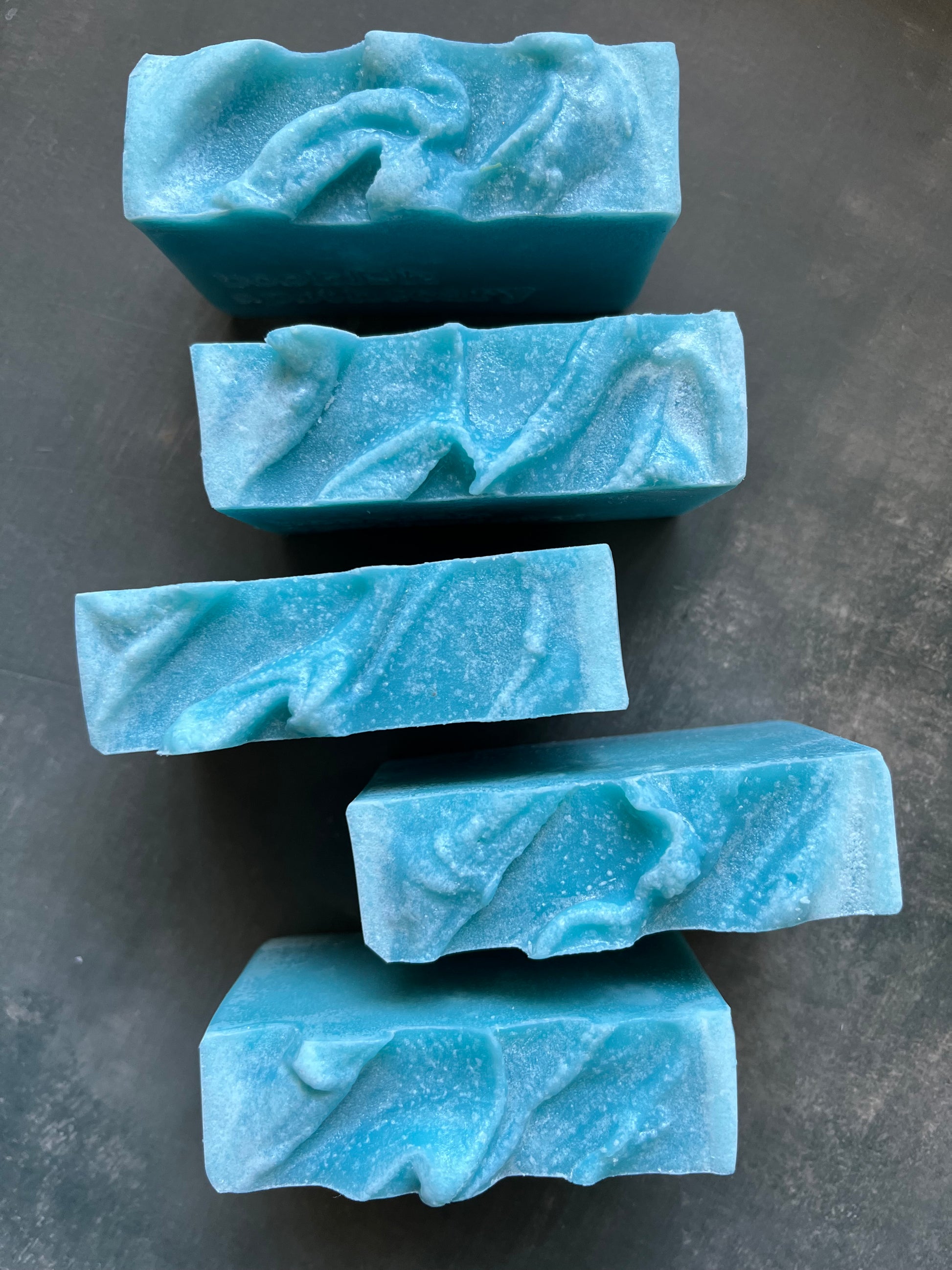 Five blue marbled soap bars on a dark gray surface