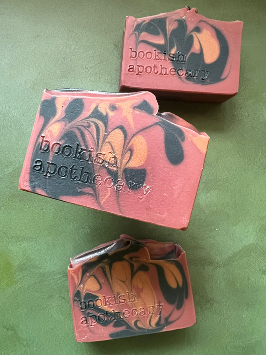 Three bars of red soap with black and bronze swirls stamped with bookish apothecary branding.