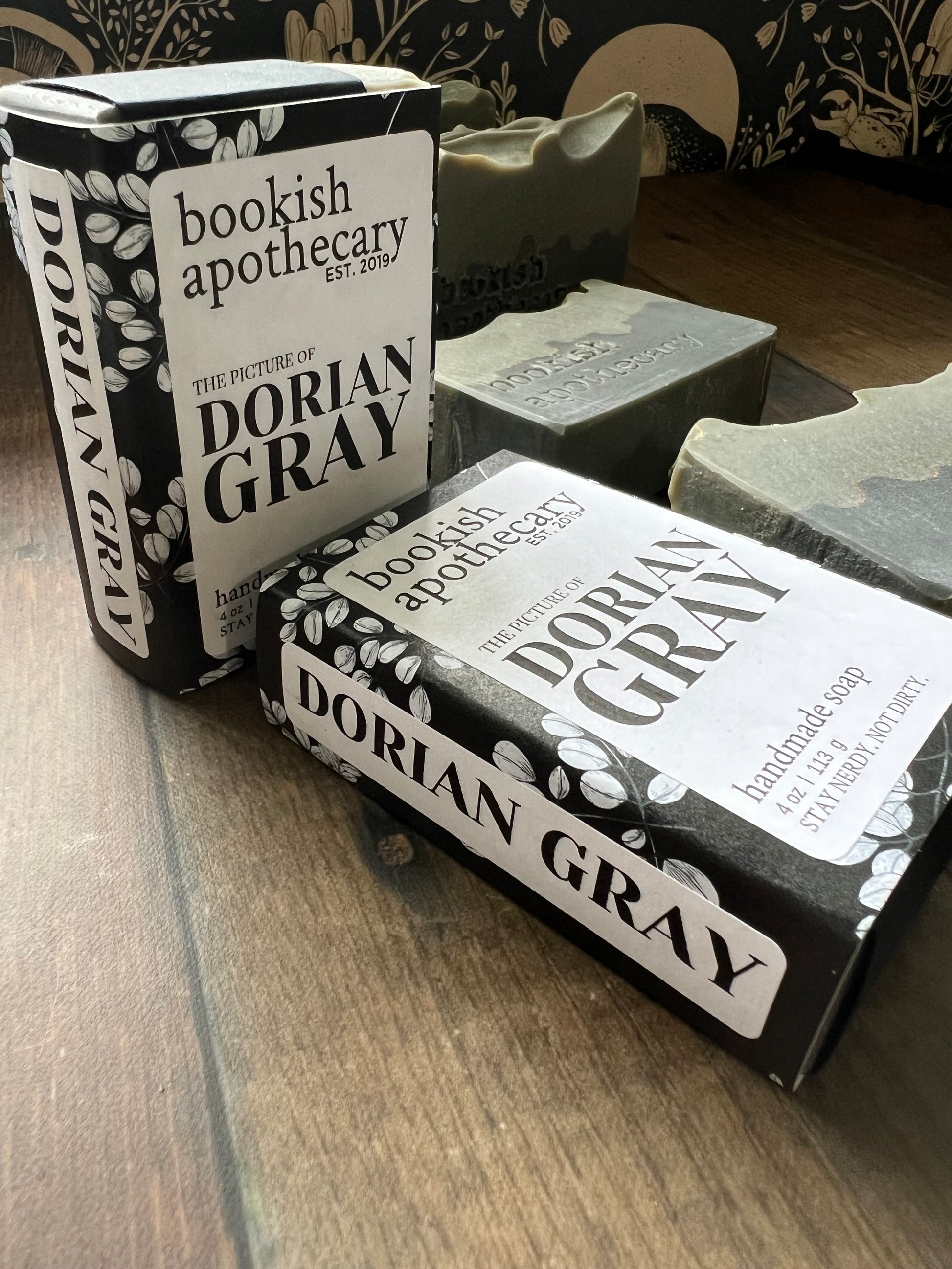 Two bars of packaged soap from 'bookish apothecary' on a wooden surface