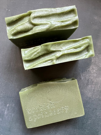 Three green soap bars on a gray surface, with one bar showing 'bookish apothecary' branding.