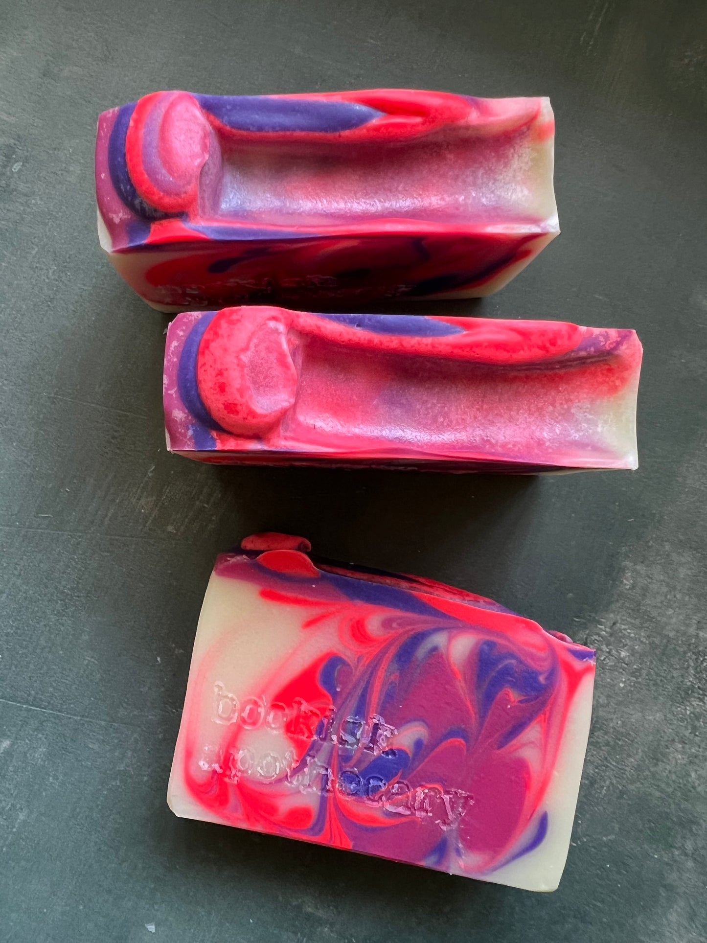 Three colorful soap bars with a marbled pattern on a dark surface