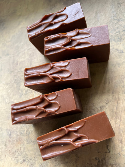 Five rectangular pieces of dark brown chocolate with embossed leaf patterns, arranged on a textured beige surface.