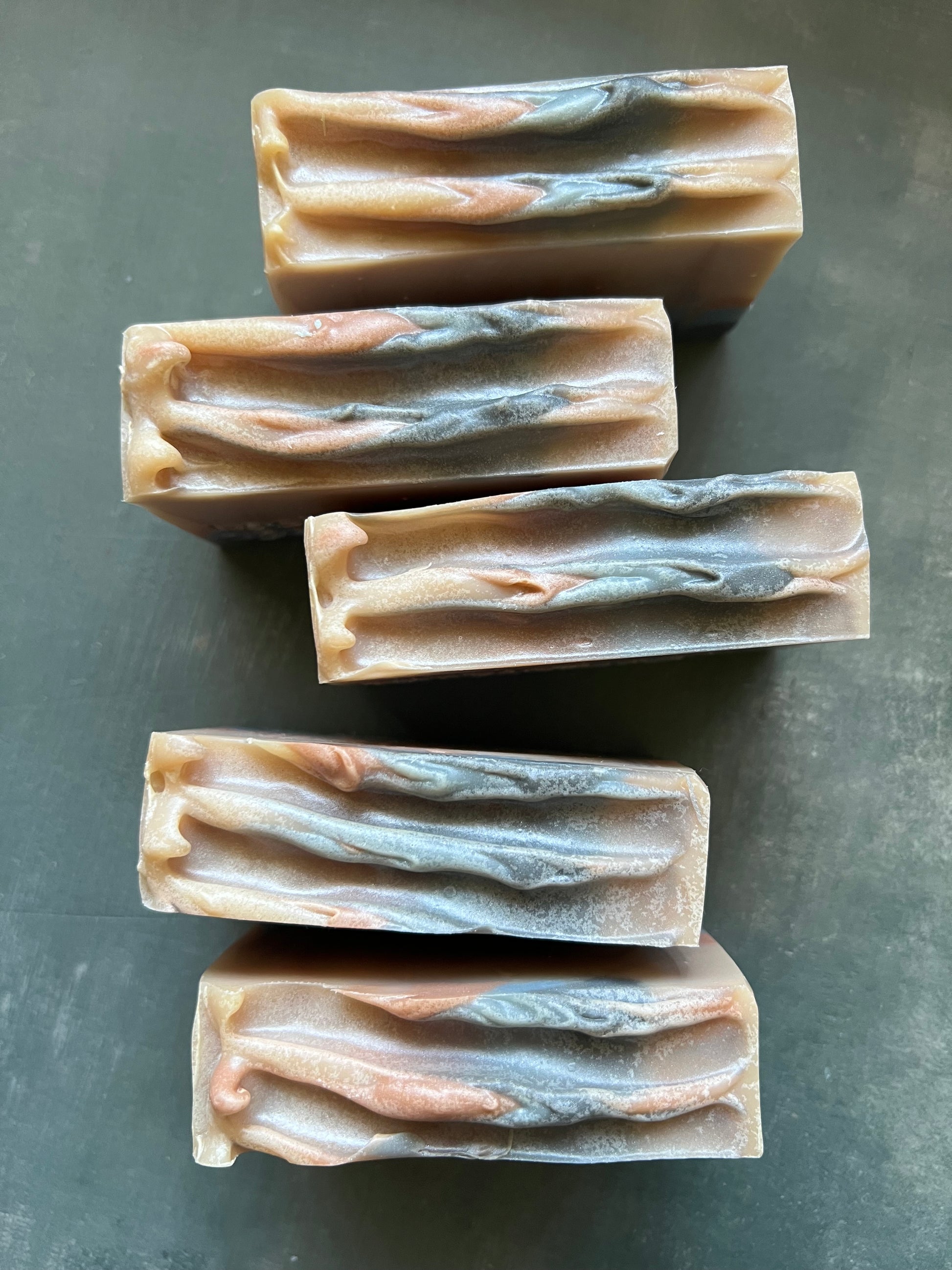 Five bars of soap with a natural, textured pattern on a dark surface