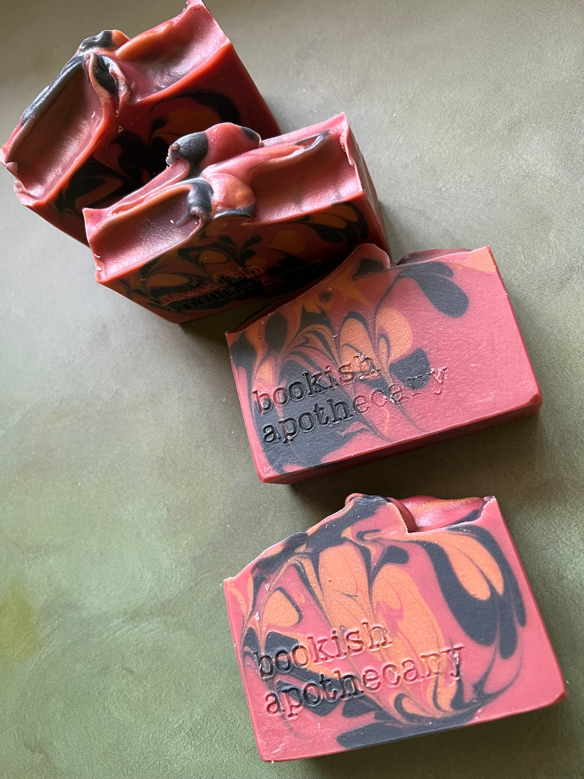 four bars of red soap with black and bronze swirls stamped with bookish apothecary branding.