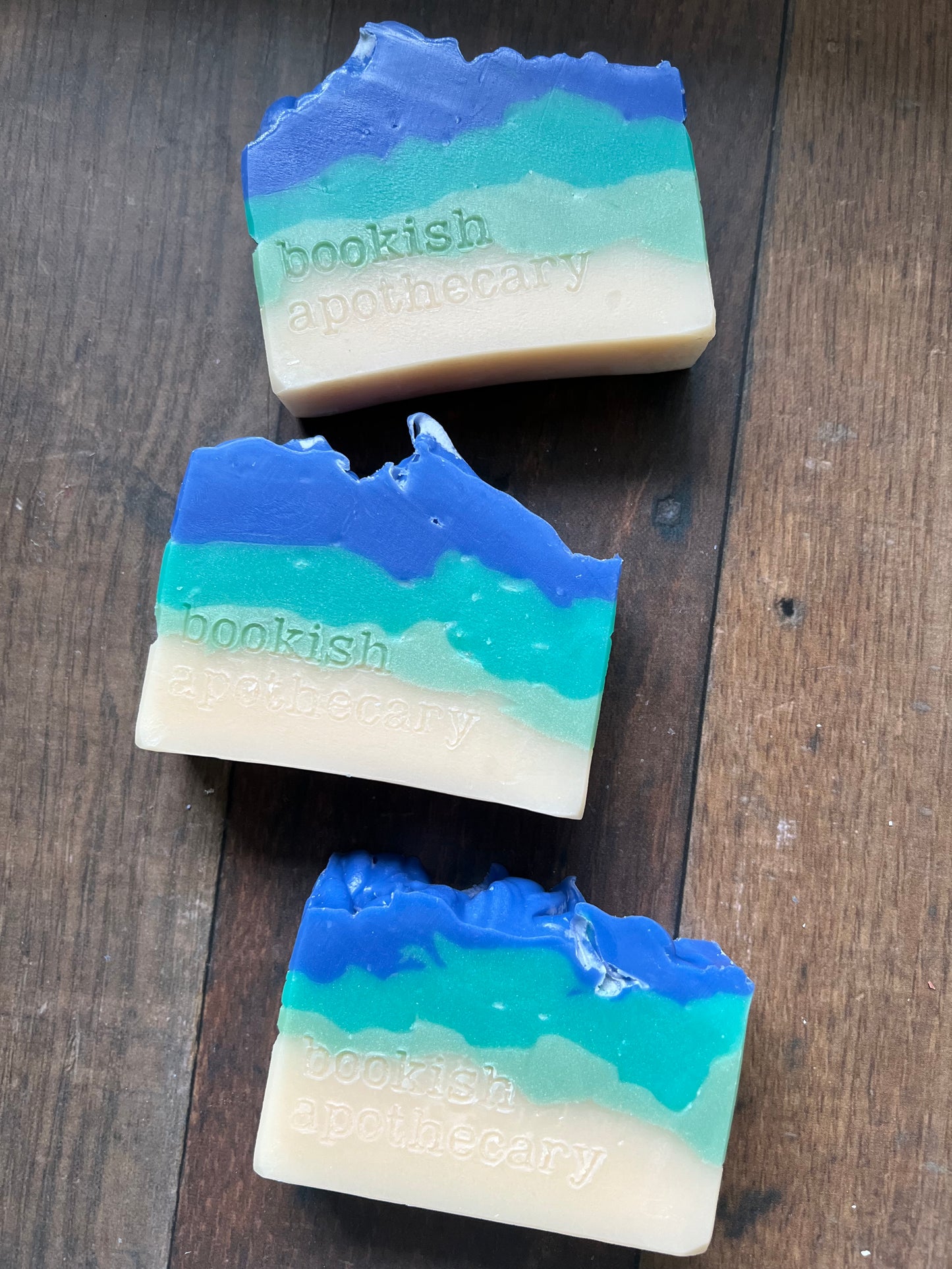 Three bars of soap with blue and green layers on a wooden surface