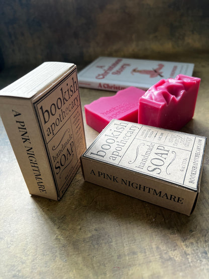 Handmade soap bars and matching paper boxes from Bookish Apothecary, featuring a pink soap bar and vintage-style typography on a rustic bronze surface.
