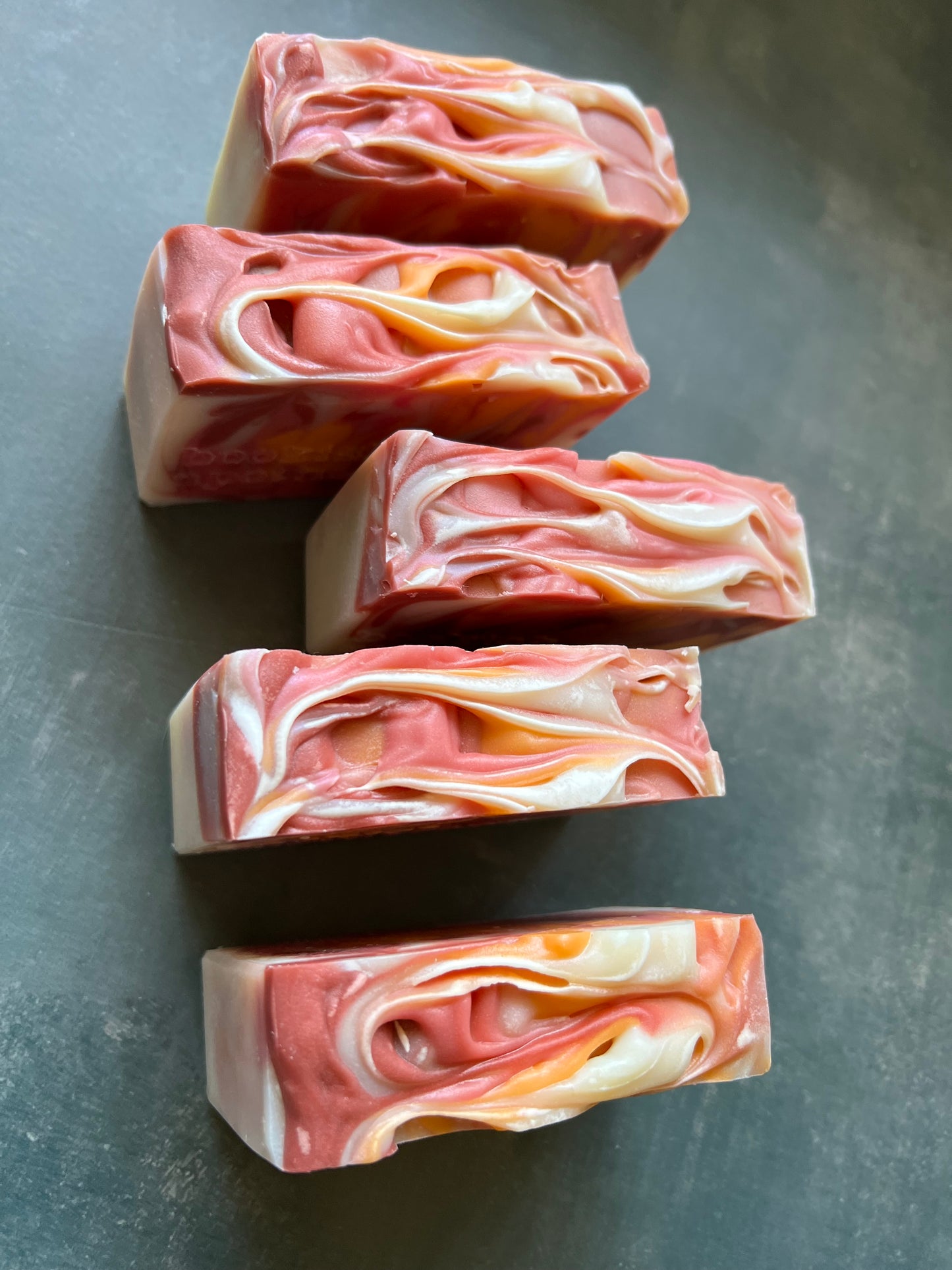 Five bars of pink and white swirled soap on a gray surface