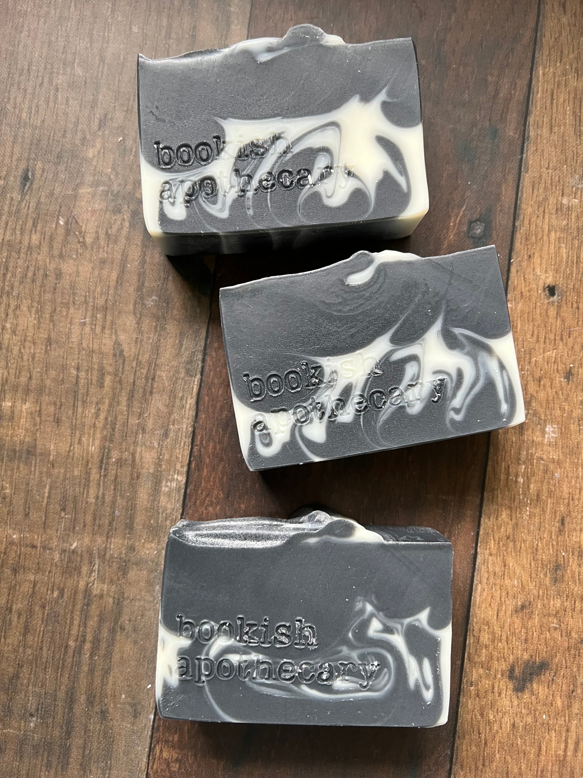 Three soap bars with marbled design on a wooden surface, branded 'bookish apothecary'.