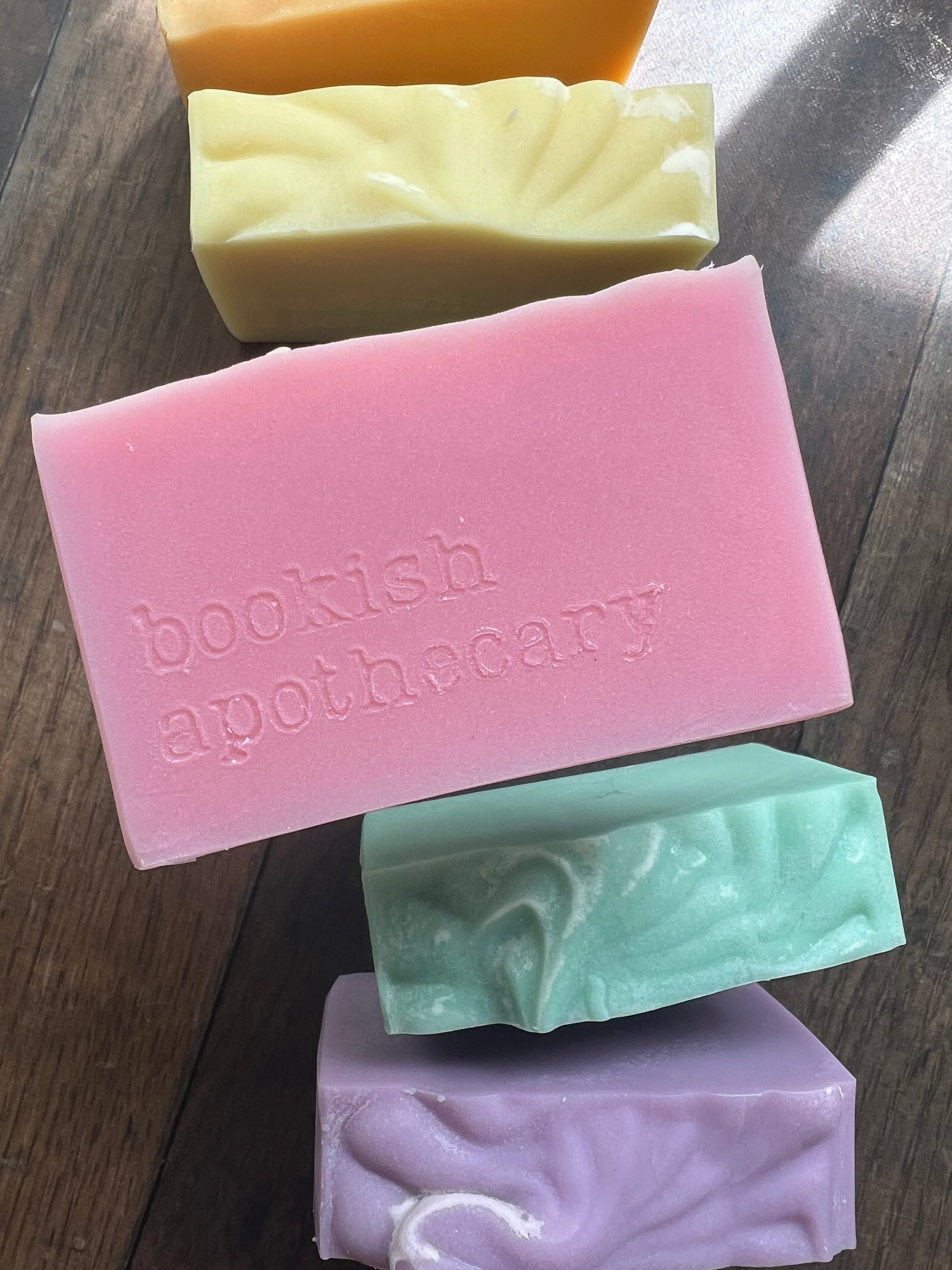 Five colorful soap bars on a wooden surface, with 'bookish apothecary' branding.