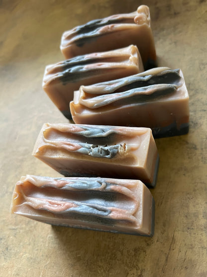 Five rectangular bars of handmade soap with a marbled pattern of beige, brown, and charcoal gray, arranged on a textured beige surface.