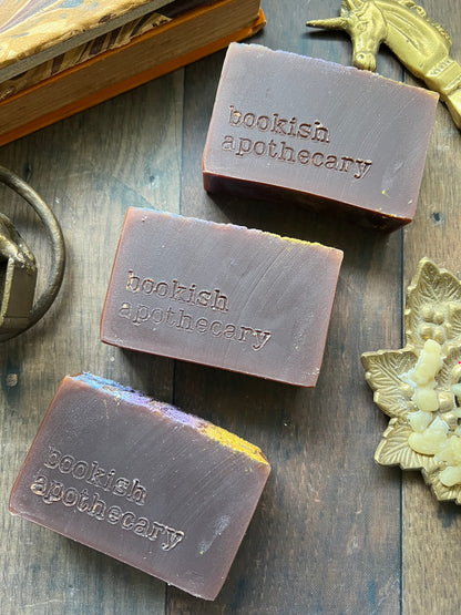 Three bars of soap from 'bookish apothecary' on a wooden surface with decorative elements.