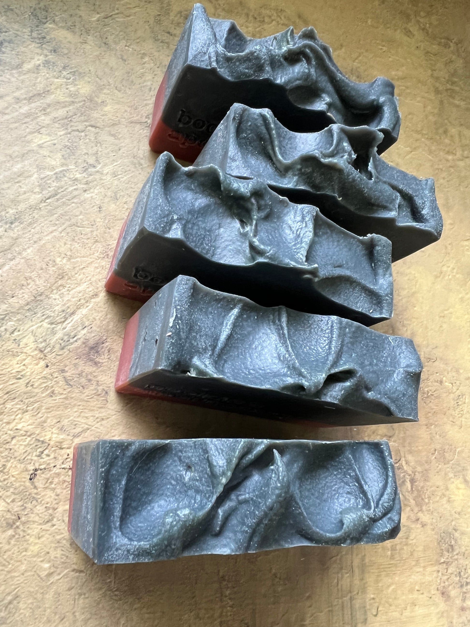 Five dark gray, textured rectangular bars with wavy, organic patterns on top, arranged on a textured tan surface.