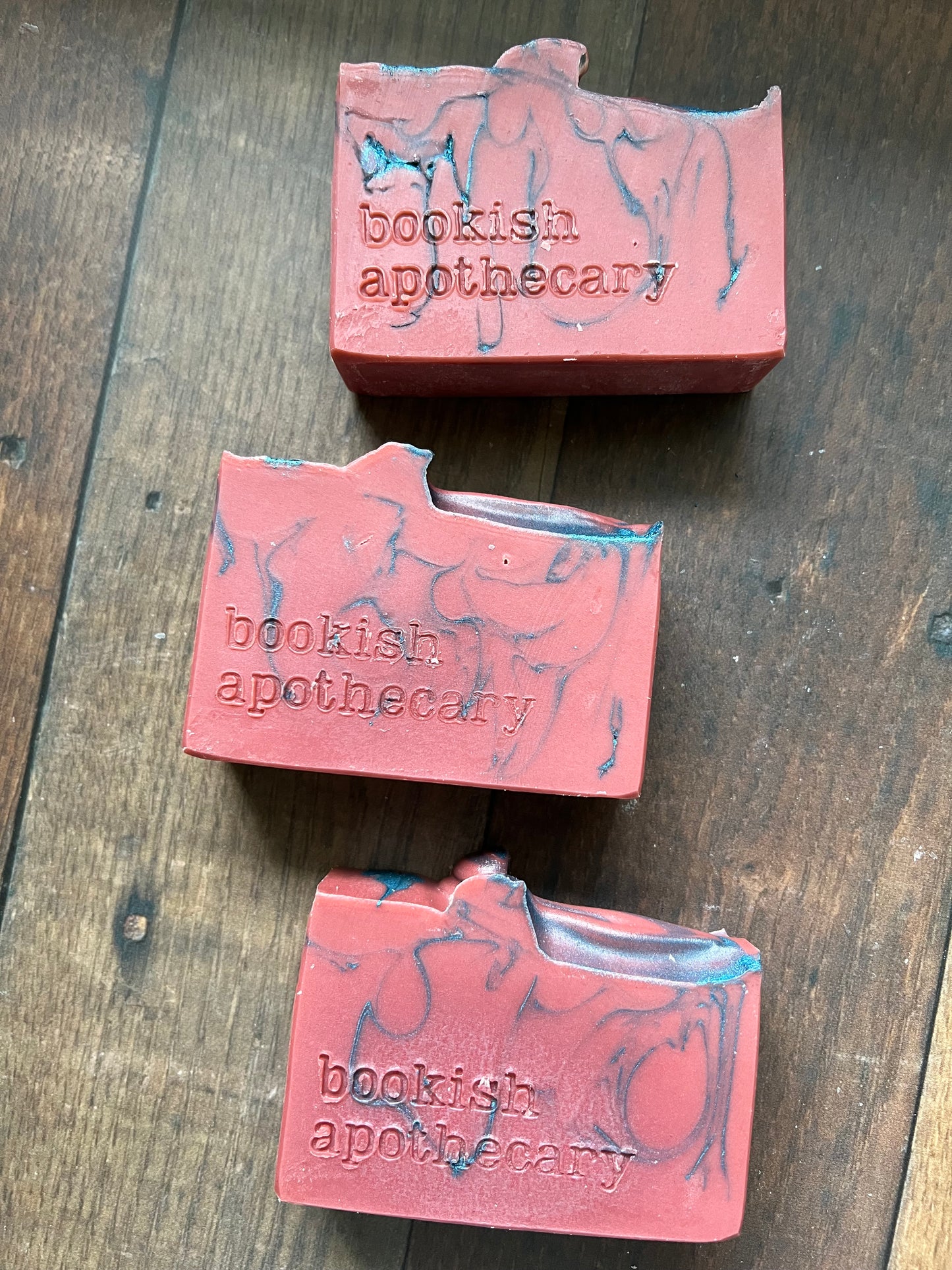 Three bars of red soap from 'bookish apothecary' on a wooden surface