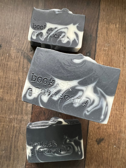 Three bars of black and white soap with 'bookish apothecary' branding on a wooden surface