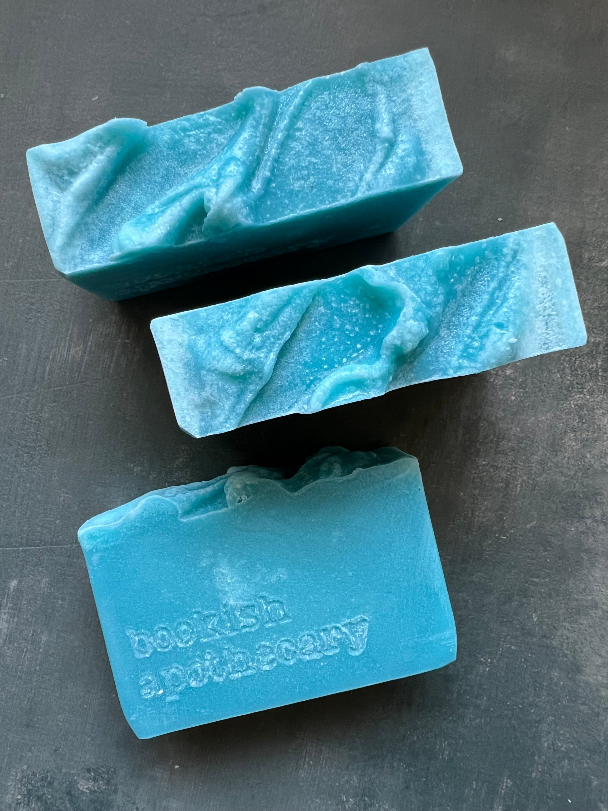 Three bars of blue soap on a dark surface