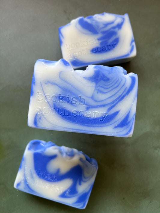 Three bars of blue and white swirled soaps stamped with bookish apothecary branding.