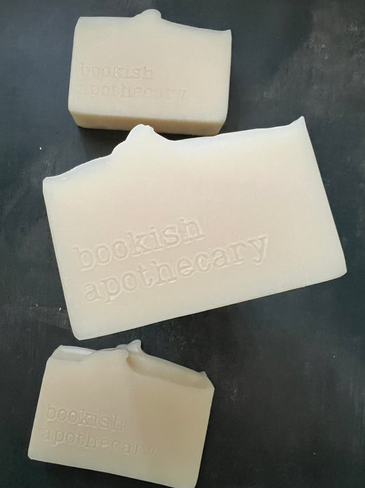 Three cream-colored solid bars of soap with embossed branding, displayed on a dark textured surface.