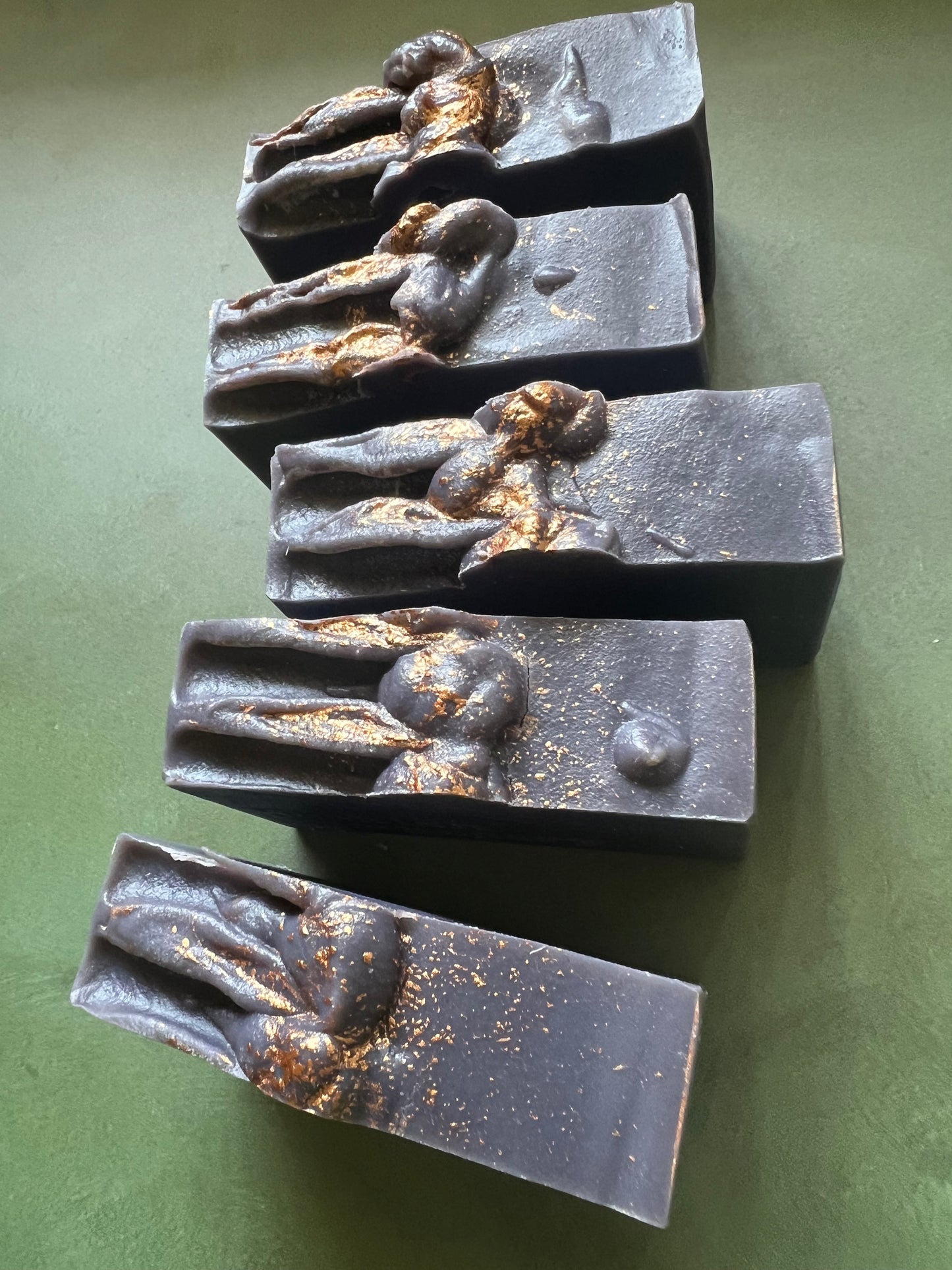 Four bars of dark purple soap with gold tops stamped with bookish apothecary branding.