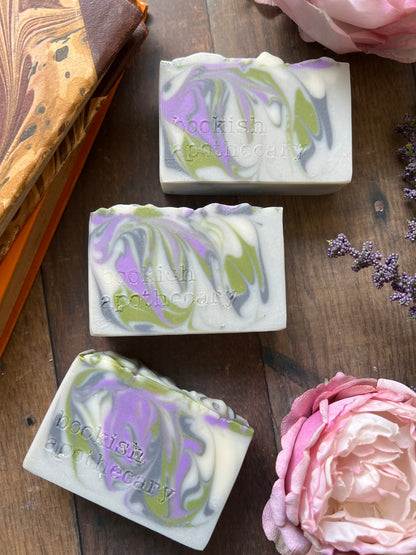 Three marbled soap bars on a wooden surface with flowers and a notebook.
