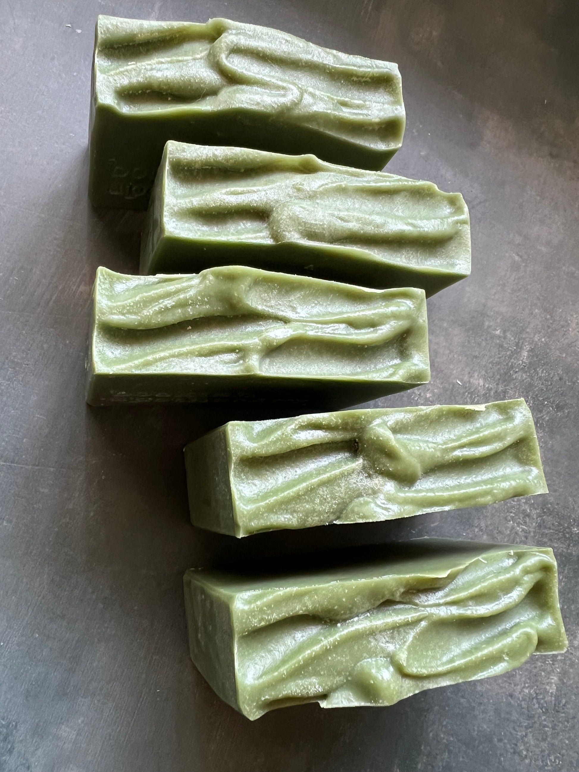 Five green soap bars with a textured surface on a gray background
