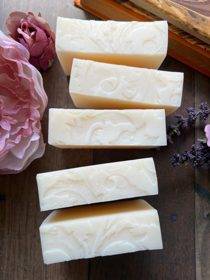 Five bars of white soap with embossed designs on a wooden surface with flowers.